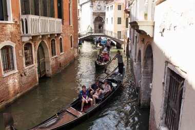 Turistler Venedik / İtalya 'daki eski tarihi binalar arasındaki kanallarda gondollara biniyorlar..