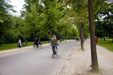Amsterdam 'daki Vondelpark' ta bisiklet süren, yürüyen, ağaç ve yol gezen insanların görüntüsü. 47 hektarlık bir halk parkı. Bu bir yaz günü..