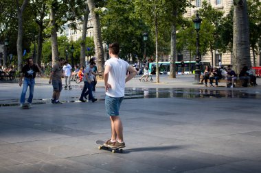 Genç erkekler Paris 'teki Cumhuriyet Meydanı' nda kayıyorlar. İnsanlar arka planda takılıyor.