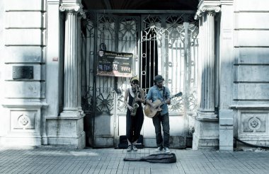 Sokak caz müzisyenleri (kadın ve erkek), Beyoğlu İstanbul 'daki Istiklal Bulvarı' ndaki tarihi bir binanın önünde saksafon ve gitar çalıyorlar. Görüntü, bölgenin kültürel özünü gösteriyor.