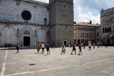 Koper / Slovenya 'daki Assumption Katedrali' nin (Stolnica Marijinega vnebovzetja) saat kulesinin önünde insanlar yürüyor. Praetorian Sarayı da manzaralı..