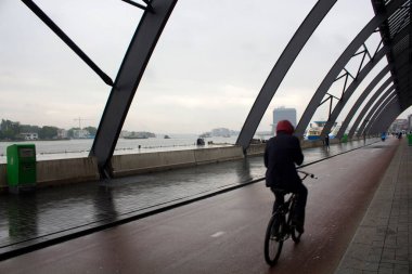 Amsterdam Centraal adlı ana tren istasyonunun arkasında bisiklet süren bir adamın bulanık görüntüsü. Yağmurlu bir yaz günü..
