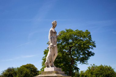 Paris 'teki Jardin Des Tuileries' deki kadın heykeli. Arka planda ağaçlar ve mavi gökyüzü var.