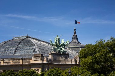 Paris 'teki Grand Palais. Binanın tepesinde Fransız bayrağı dalgaları var. Sanat galerisi 1900 'de inşa edildi, sergiler ve kültürel etkinlikler düzenlendi. Georges Recipon 'un heykeli manzarada.