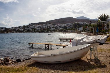 Sonbaharda Bodrum yarımadasındaki Turkbuku köyünde boş sahil, küçük rıhtım ve küçük beyaz tekne manzarası. Görüntü, turizm krizlerinin bölgeyi nasıl etkilediğini de gösteriyor.