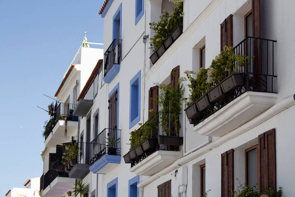 View of traditional, white, typical buildings in Ibiza. The image reflects architectural style of island. Iron made railings and many plants on balconies are in scene.