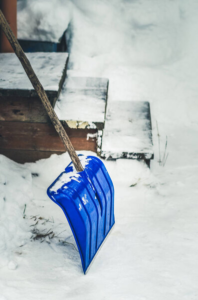 Blue snow shovel cleans sidewalks and stairs in winter season