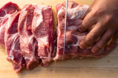 Ahşap arka plan üzerinde havai görünümü domuz ham parçasının. Bir parça taze kemiksiz domuz, boyun bölümü veya yaka. Büyük siyah bir zemin üzerine kırmızı çiğ et parçası. Kasap eller yakın çekim: ahşap tahta kesme karşılamak