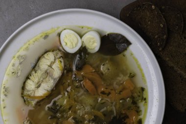 Sebze, pirinç, otlar ve küçük yumurta beyaz plaka ile balık çorbası. Taze balık çorbası malzemeler ve baharat ekmek ile. Gri arka plan