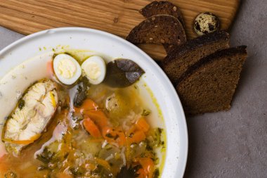 Sebze, pirinç, otlar ve küçük yumurta beyaz plaka ile balık çorbası. Taze balık çorbası malzemeler ve baharat ekmek ile. Gri arka plan