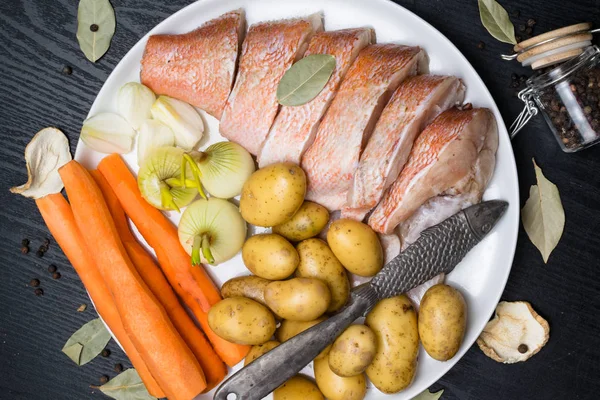 Uncooked sea perch, with fish spices, carrot, potatoes, pepper, onion, bay leaf, celery on dark background. Healthy food and diet concept. Ingredients for cooking fish