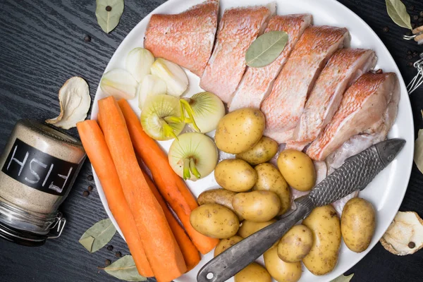 Uncooked sea perch, with fish spices, carrot, potatoes, pepper, onion, bay leaf, celery on dark background. Healthy food and diet concept. Ingredients for cooking fish