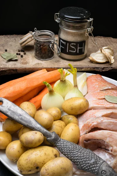 Uncooked sea perch, with fish spices, carrot, potatoes, pepper, onion, bay leaf, celery on dark background. Healthy food and diet concept. Ingredients for cooking fish