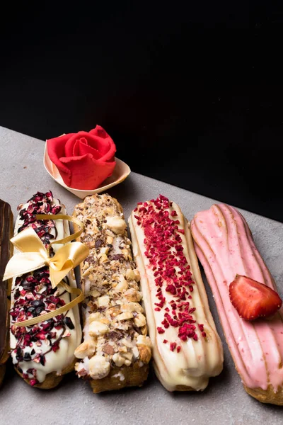 Tatlı lezzetli renkli Fransız eklerleri. Fransız tatlı grubudur. Pasta arka plan. Fransız pasta eklerleri ahududu ile dekore edilmiş, sırlı, krema, çikolata, badem ezmesi yükseldi. Yay ile çeşitli seçimi