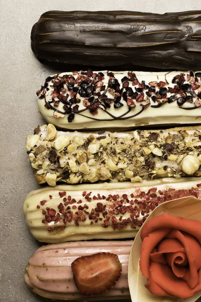 Tatlı lezzetli renkli Fransız eklerleri badem ezmesi kırmızı gül ile dekore edilmiştir. Fransız tatlı grubudur. Pasta arka plan. Fransız pasta eklerleri ahududu, krema ve çikolata ile dekore edilmiş, sırlı. Çeşitli seçimi