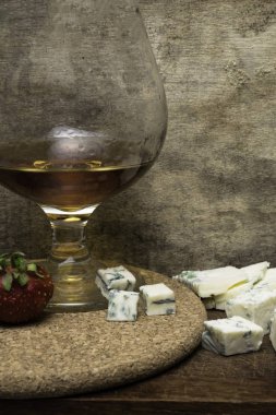 Konyak ve Fransız mavi peynir bir ahşap tahta üzerinde natürmort. Cam Konyak, peynir, ahşap arka plan üzerinde çilek ile