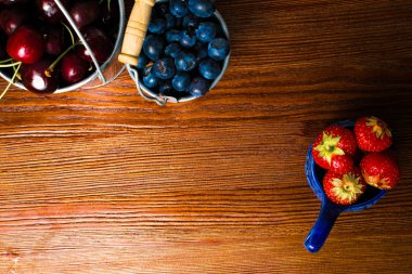 Ahşap arka plan üzerinde meyveleri. Yaz veya bahar organik Berry üzerinde ahşap metal kovalar. Çilek, yaban mersini ve kiraz tarım, bahçecilik, kavram hasat