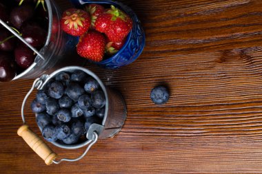 Ahşap arka plan üzerinde meyveleri. Yaz veya bahar organik Berry üzerinde ahşap metal kovalar. Çilek, yaban mersini ve kiraz tarım, bahçecilik, kavram hasat
