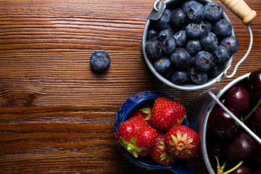 Ahşap arka plan üzerinde meyveleri. Yaz veya bahar organik Berry üzerinde ahşap metal kovalar. Çilek, yaban mersini ve kiraz tarım, bahçecilik, kavram hasat