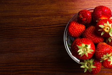 Ahşap masa üzerinde taze çekilmiş çilek ile küçük cam kase