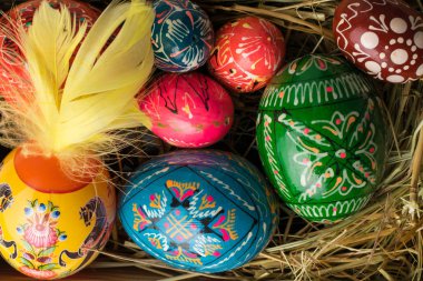 Paskalya yumurta ve tüyler saman ahşap arka plan üzerinde renkli