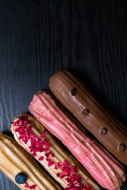 Fransız geleneksel C'eclair, ahududu, yaban mersini, krem, kahve fasulye siyah arka plan üzerine dekore