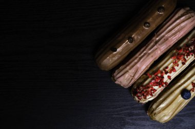 Fransız geleneksel C'eclair, ahududu, yaban mersini, krem, kahve fasulye siyah arka plan üzerine dekore