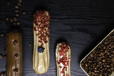 kahve çekirdekleri, yaban mersini, siyah ahşap masa üzerinde ahududu ile lezzetli renkli eklerleri