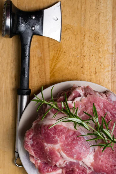 Pieces of raw pork steak with rosemary and butcher hummer, on dark wooden background in rustic style