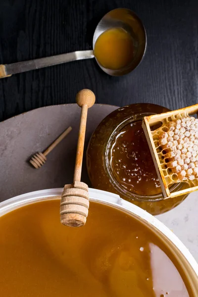 Med ve sklenici a velký kbelík, honeycomb a dřevěnou tyčí, kovová naběračka — Stock fotografie