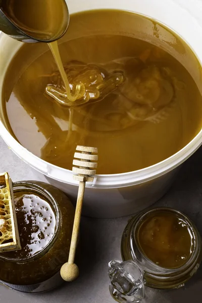 Med ve sklenici a velký kbelík, honeycomb a dřevěnou tyčí, kovová naběračka — Stock fotografie