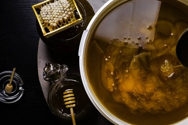 Verse honing in witte emmer en in glazen pot, met honingraat, houten stokken — Stockfoto