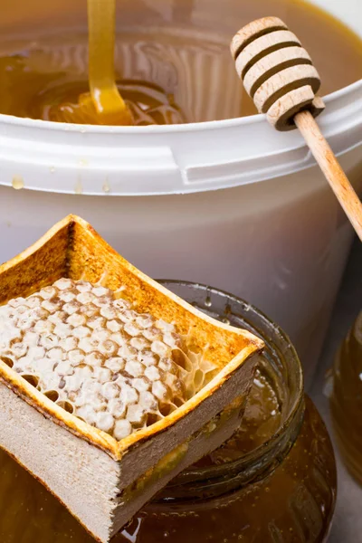 Med ve sklenici a velký kbelík, honeycomb a dřevěnou tyčí — Stock fotografie