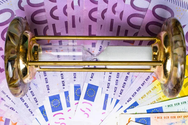 many 500 euro banknotes background with hourglass. EU currency, save money and time concept