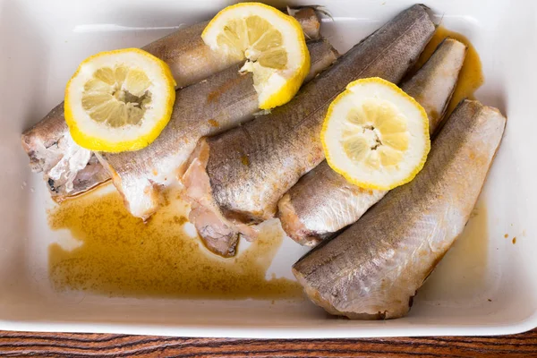 filleting hake fish raw with lemon, spices in cooking pan