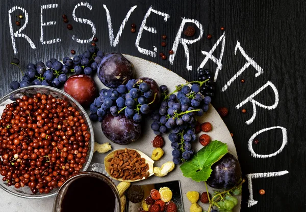 yiyecek zengin resveratrol, üzüm, Erik, goji, fıstık, kızılcık, raspberrys koyu çikolata, siyah ahşap zemin üzerine kırmızı şarap