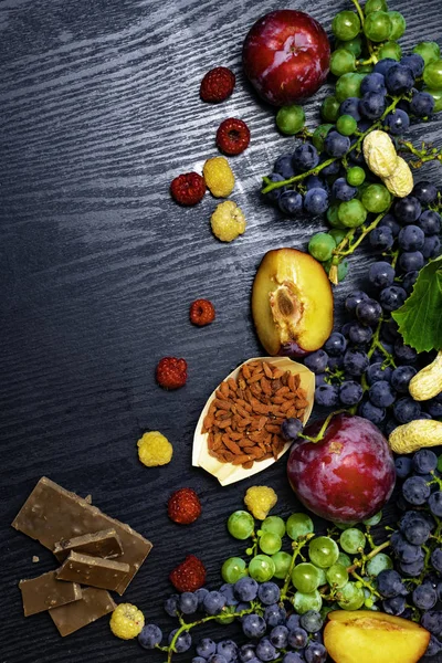 Cibo ricco di resveratrolo, uva, prugne, goji, arachidi, mirtilli rossi, lamponi cioccolato su fondo di legno nero — Foto Stock