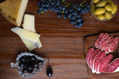 Farklı aperatifler ve mezeler karışımı. İspanyolca tapas bir ahşap plaka üzerinde. Tapas bar. Chorizo, yeşil ve siyah zeytin, sosis, peynir, mavi üzüm. Üstten görünüm