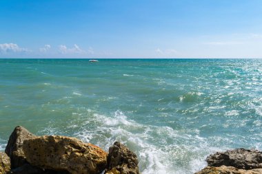 arka plan mavi-yeşil parlak sarı taşlar üzerinde sörf dalga deniz. Mavi deniz ve kıyı ve yat, gevşeme güneşli bir günde sprey