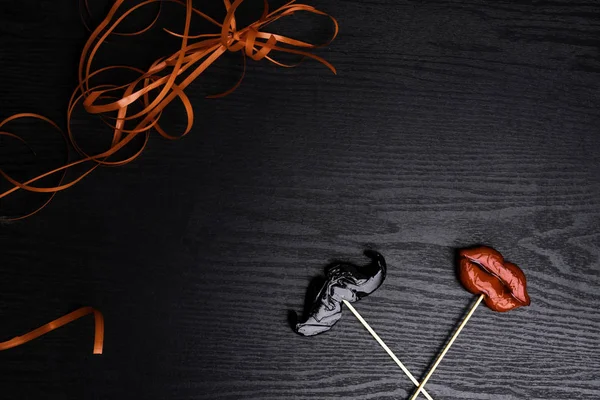 close up of mustache and female red lips made candy, decorated with red ribbon on black wooden background, weeding and love concept