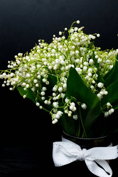 Lily of the valley flowers in glass vase, black background, selective focus, spring mood