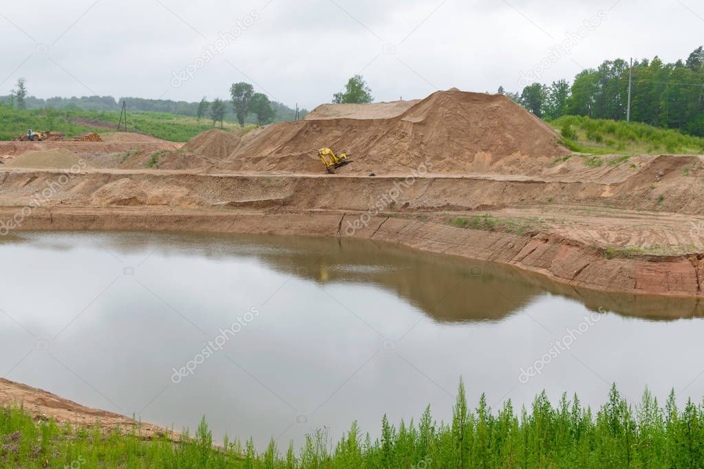 yellow excavator and tractor at sandpit with water during earthmoving works