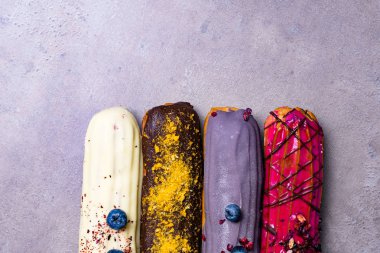 Tatlı ve berry Fransız tatlı pasta menekşe arka plan üzerinde grup ile renkli eklerleri. Kremalı pasta tatlı içinde krem şanti ile