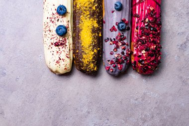 Tatlı ve berry Fransız tatlı pasta menekşe arka plan üzerinde grup ile renkli eklerleri. Kremalı pasta tatlı içinde krem şanti ile