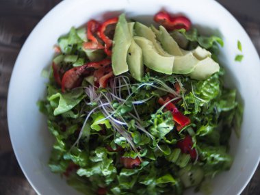 Fresh vegetable salad with cucumber, lettuce, avocado, green sprouts, bell pepper on white plate. Bowl of salad with vegetables on newspaper, selective focus