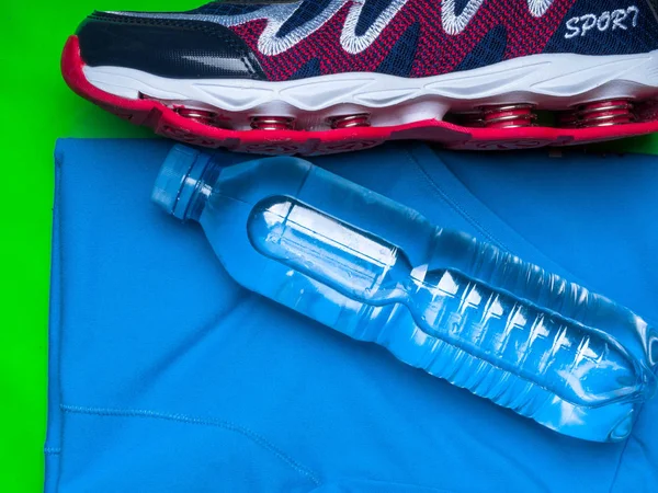 Sports runner shoe, shirt and a bottle of water on green sport mat, copy space