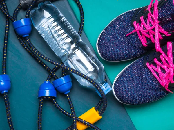 sport set with women sneakers, expander, bottle of water on green mat