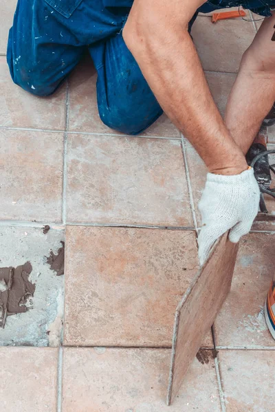 The hands of the tiler are laying the ceramic tile on the floor outdoor