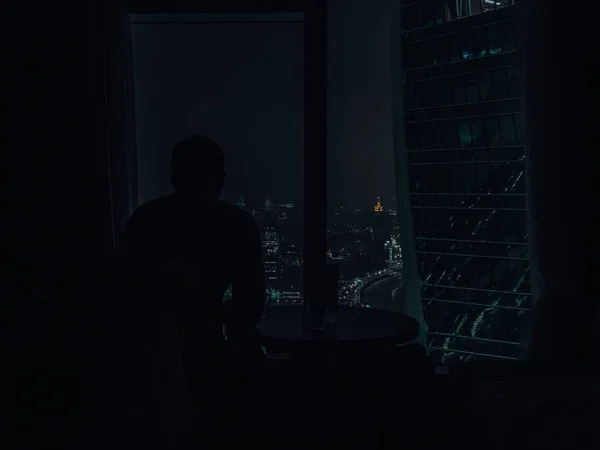 Silhouette Man mirando al hermoso color de la luz nocturna de la ciudad desde la ventana moderna del rascacielos por la noche — Foto de Stock