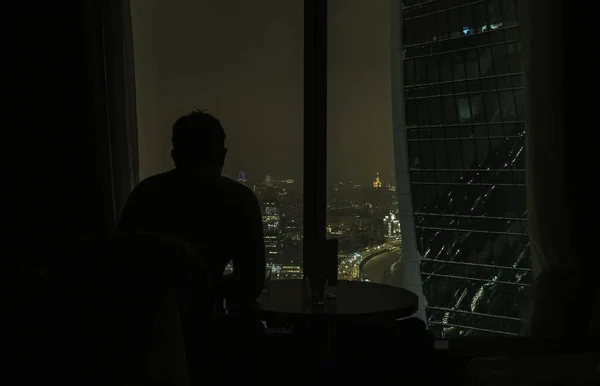 Silhouette Man mirando al hermoso color de la luz nocturna de la ciudad desde la ventana moderna del rascacielos por la noche — Foto de Stock